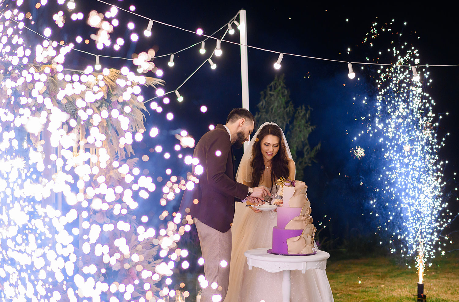 Newlyweds cutting their cake between firework fountains